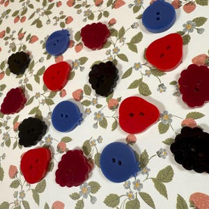 May include: Assortment of colorful buttons in various shapes, including berries, strawberries, and circles. The buttons are made of plastic and have a glossy finish.