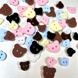 May include: Assortment of colourful bear-shaped buttons in various colours including pink, blue, brown, black, and cream.