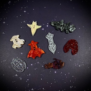 May include: Assortment of nine colorful, unique buttons with various shapes and designs. The buttons are made of different materials, including wood, plastic, and metal. The buttons are perfect for adding a touch of personality to any project.