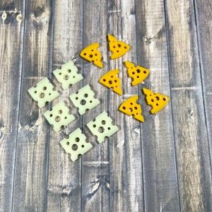 May include: A collection of yellow and white cheese-shaped ornaments on a wood background. The ornaments are in the shape of triangles and squares.
