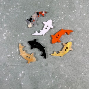May include: Six colorful fish-shaped buttons with two holes each. The buttons are made of plastic and have a glossy finish. The colors include black, white, orange, and brown.