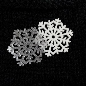 May include: Two white snowflake ornaments, one with a glitter finish and the other with a smooth surface, against a black background.