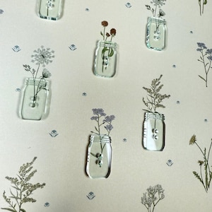 May include: Nine clear glass jars with different dried flowers and plants inside. The jars are arranged in a grid pattern on a beige background with a floral pattern.
