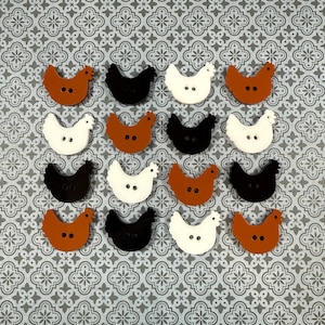 May include: A collection of decorative buttons shaped like chickens. The buttons are in various colors, including white, black, and shades of brown. Each button has two small holes for sewing. The buttons are arranged on a patterned background.