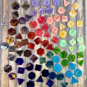 May include: A collection of colorful, geometric buttons in various shapes, including hexagons, squares, and triangles. The buttons are arranged on a wooden surface, showcasing a spectrum of colors from purple to blue, green, yellow, orange, and red.