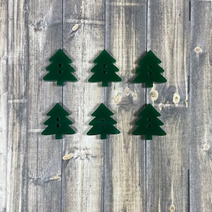 May include: Six dark green Christmas tree shaped buttons on a wood background.