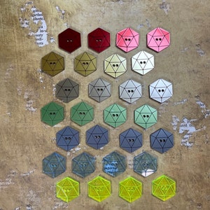 May include: A collection of 20 hexagonal-shaped buttons in various colors, including red, pink, gold, silver, green, blue, and yellow. The buttons have a raised, geometric design and are arranged in rows on a textured background.