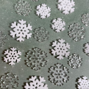 May include: A collection of white and silver snowflake ornaments. The snowflakes are various sizes and have a 3D design.