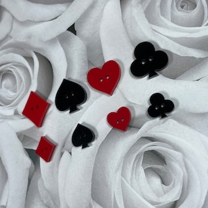 May include: A collection of red and black felt buttons shaped like hearts, spades, and clubs. The buttons are arranged on a white background.