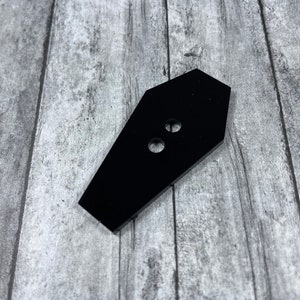 Peut inclure: Bouton noir en forme de cercueil avec deux trous.