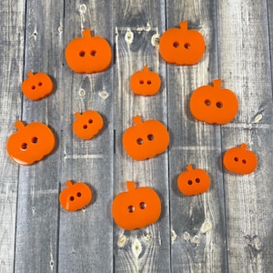 May include: A set of 12 orange pumpkin-shaped buttons. The buttons are various sizes and are perfect for crafting projects.
