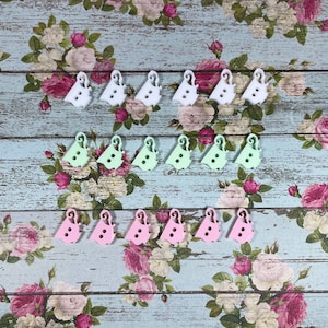 May include: Assortment of pastel-coloured plastic buttons in the shape of a bird. The buttons are arranged in three rows on a floral patterned background.