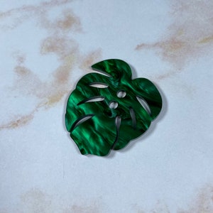 May include: A green, marbled, plastic button shaped like a monstera leaf.