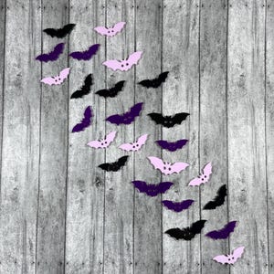 May include: A collection of purple and pink bat-shaped decorations arranged in a diagonal line on a gray wooden background.