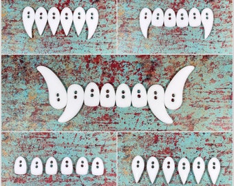 May include: A set of white plastic teeth, arranged in different configurations on a blue and red textured background. The teeth are shaped like fangs and have a rounded, smooth surface.