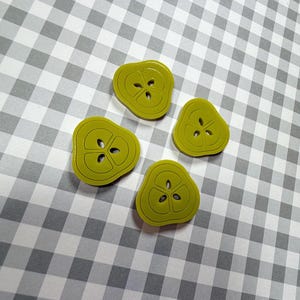 May include: Four lime green pear-shaped buttons with a three-hole design. The buttons are arranged on a gray and white checkered background. The buttons have a glossy finish and a dark green outline.