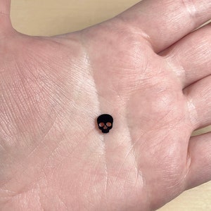 May include: A small black skull charm, perfect for adding a touch of gothic style to jewelry or crafts.