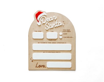 Puede incluir: Un letrero de madera arqueado con un icono de gorro de Papá Noel rojo y blanco y el texto Dear Santa. Incluye secciones de acrílico blanco para rellenar el año, la edad, el comportamiento, el deseo navideño y una línea para firmar con Love.