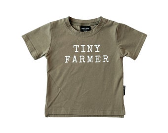 Puede incluir: Una camiseta de manga corta de color verde caqui con el texto "TINY FARMER" impreso en blanco en la parte delantera.