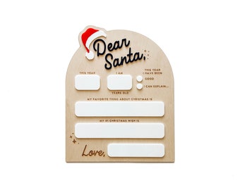Puede incluir: Un letrero de madera en forma de arco con el texto Dear Santa y un gorro de Papá Noel rojo y blanco. Incluye secciones rectangulares blancas para rellenar el año, la edad, el deseo y el nombre, además de dos círculos para marcar opciones.