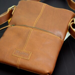 以下が含まれることがあります： 前面にジッパーポケットと「Radbags」というエンボス加工が施された、茶色の革製のクロスボディバッグです。