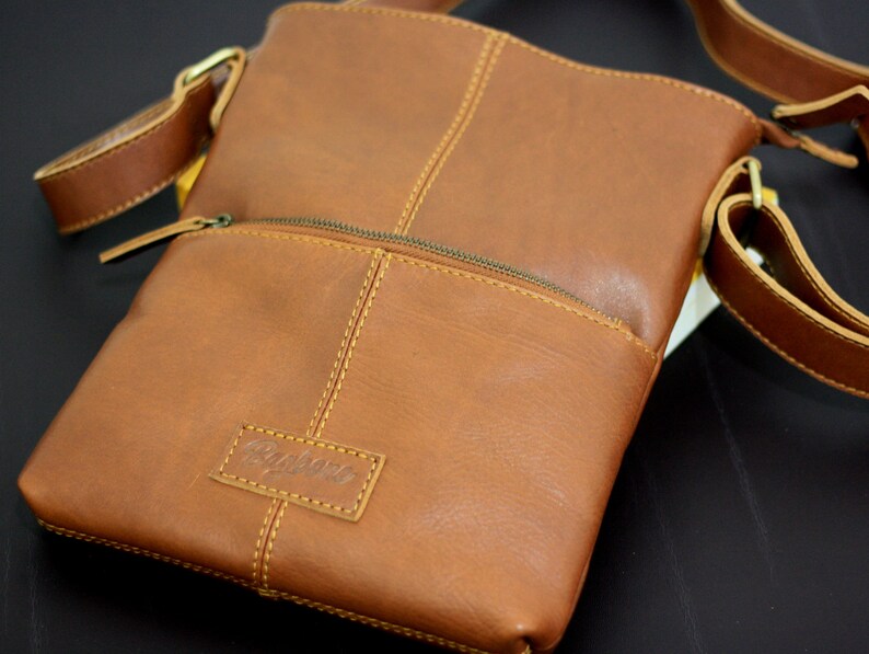 以下が含まれることがあります： 前面にジッパーポケットと「Radbags」というエンボス加工が施された、茶色の革製のクロスボディバッグです。