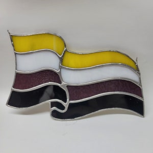 Peut inclure: Un drapeau en vitrail avec un design ondulé. Le drapeau présente des rayures horizontales jaunes, blanches, violet foncé et noires, avec des bordures métalliques argentées. Le drapeau est affiché sur un fond blanc.