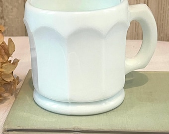 May include: A white milk glass mug with a rounded handle. The mug has a textured, octagonal design.