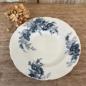 May include: A white ceramic soup bowl with a blue and white floral design. The bowl has a scalloped edge and a slightly raised rim.