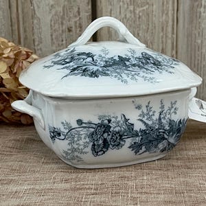 May include: A white porcelain butter dish with a lid and two handles. The dish is decorated with a blue and white floral pattern.