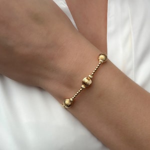 Peut inclure: Un bracelet en or avec une chaîne et des perles rondes texturées.