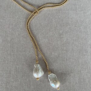 May include: A gold chain necklace with two large white pearl pendants.