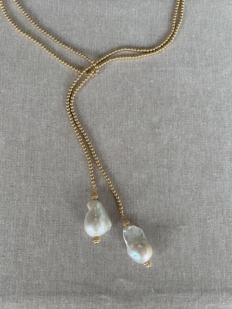 May include: A gold chain necklace with two large white pearl pendants.