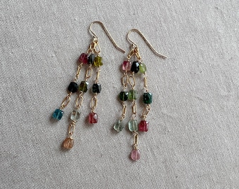 May include: A pair of gold earrings with multiple strands of small, colorful gemstone beads. The beads are in shades of green, blue, pink, and black.