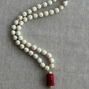 May include: A white beaded necklace with a gold clasp and a red coral pendant.