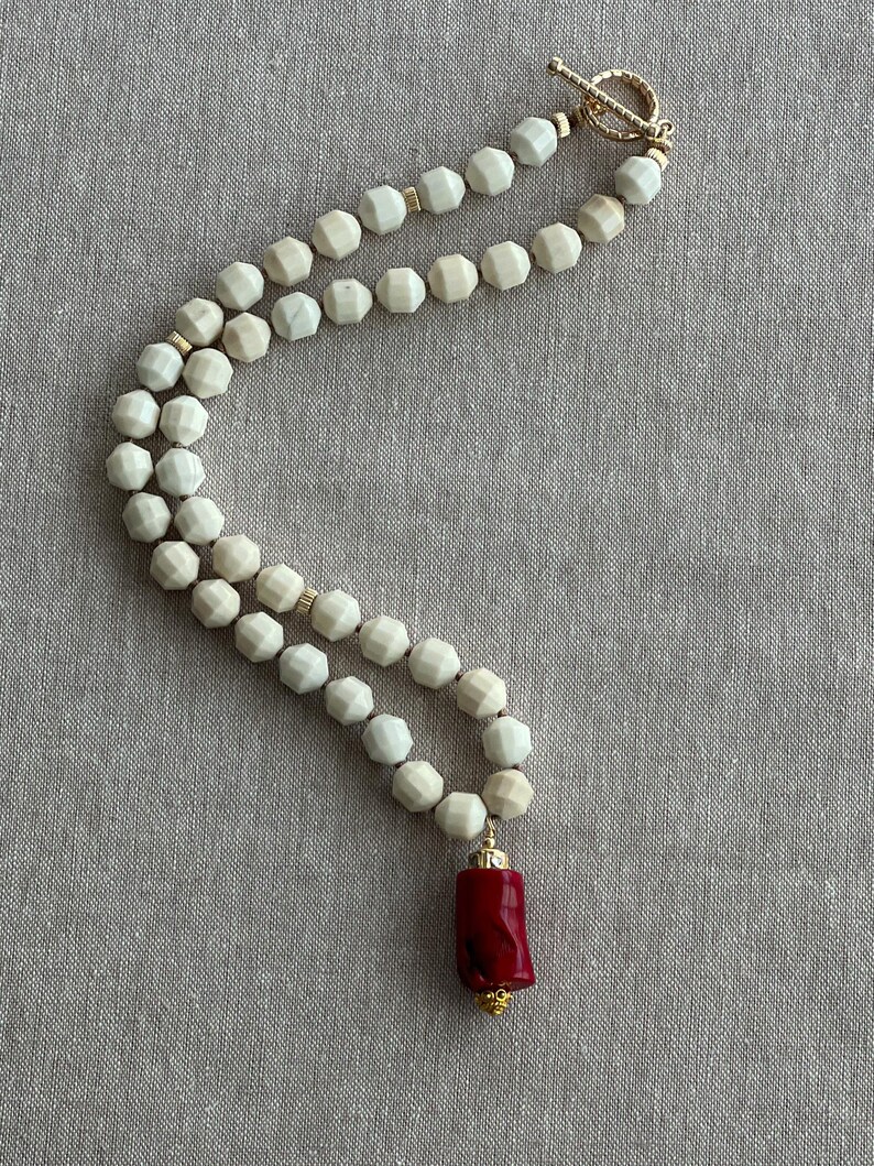 May include: A white beaded necklace with a gold clasp and a red coral pendant.