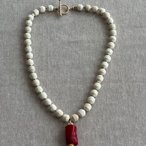 May include: A white ceramic bead necklace with a gold clasp and a red coral pendant.