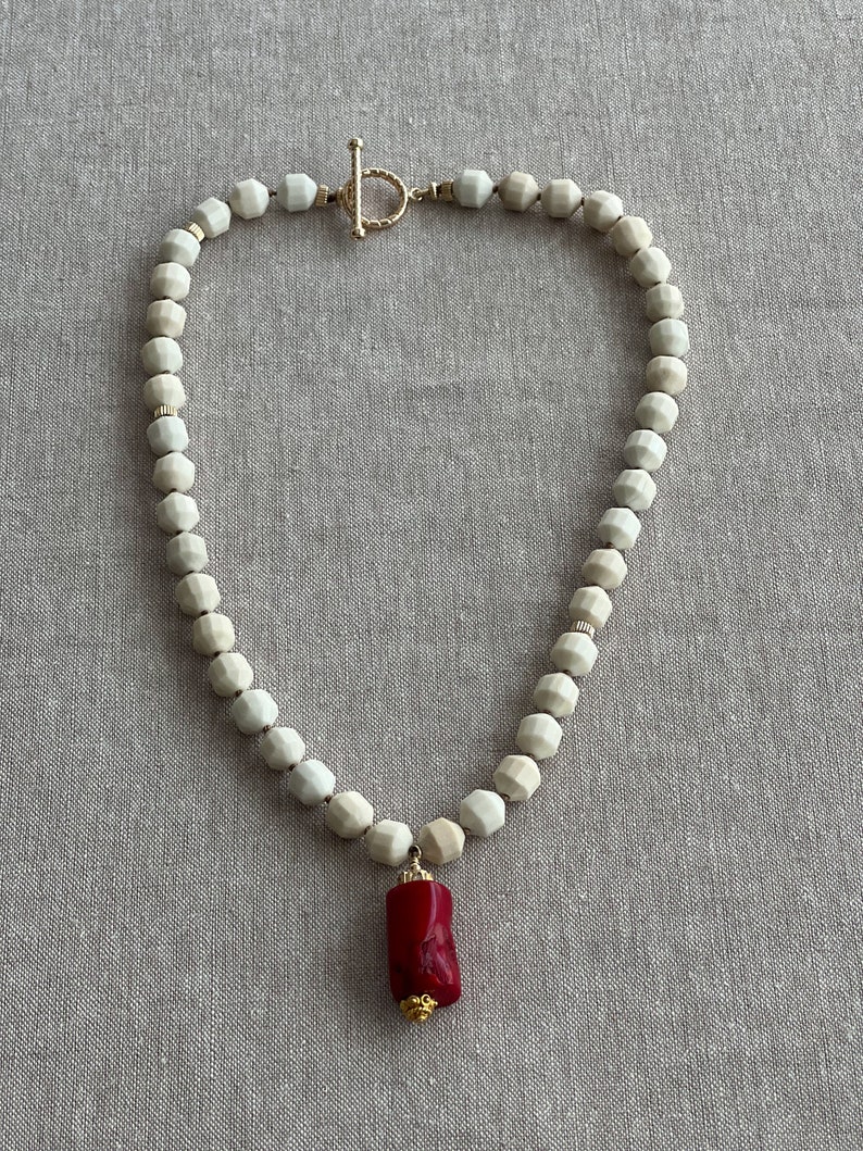 May include: A white ceramic bead necklace with a gold clasp and a red coral pendant.