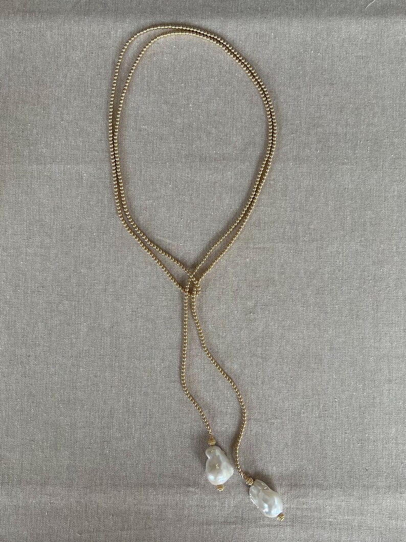 May include: A gold chain necklace with two large white pearl pendants.