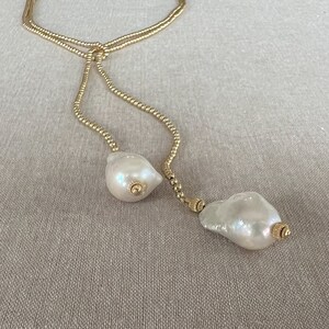 May include: A gold chain necklace with two large white baroque pearls at the ends. The chain is made of small gold beads.
