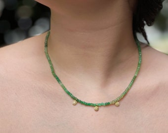 May include: A green gemstone necklace with three gold charms. The necklace is made of small, round beads and the charms are in the shape of a flower.