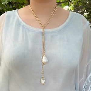May include: A long gold chain necklace with two large white pearl pendants. The necklace is layered and has a delicate gold chain.