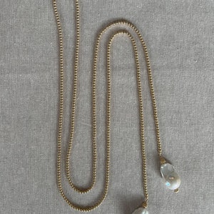 May include: A long gold chain necklace with two large white pearl pendants.