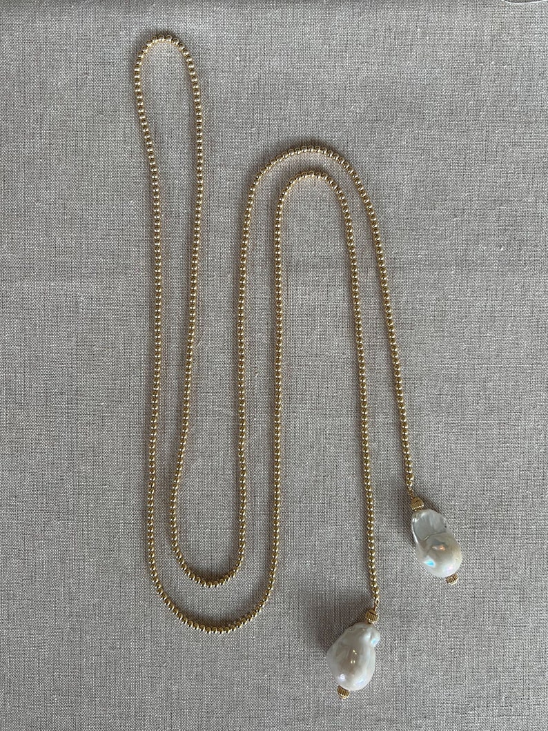 May include: A long gold chain necklace with two large white pearl pendants.