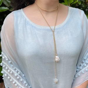 May include: A long gold chain necklace with two large white pearl pendants. The necklace is layered with a shorter gold chain.
