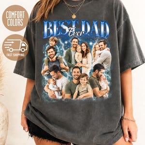 May include: A charcoal gray short-sleeve t-shirt featuring a graphic print with the text BEST DAD EVER in blue lettering. The design includes a collage of multiple photographs showing a father with his children, surrounded by a blue lightning effect.