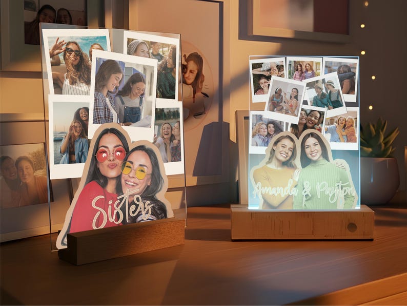 May include: Two custom acrylic photo displays with wooden bases. The left display features a collage of photos and a cutout of two people with the word Sisters. The right display shows a photo collage and a cutout of two people with the text Amanda & Payton.