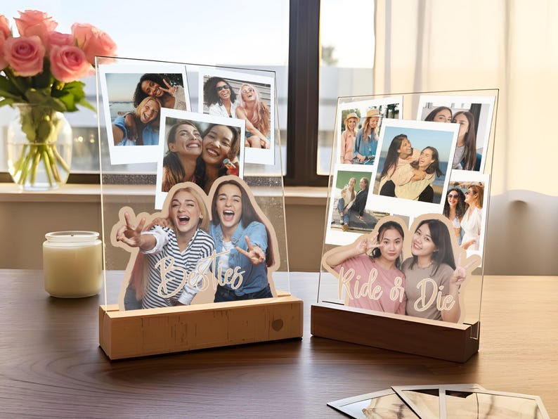 May include: Two clear acrylic photo displays with wooden bases. The left display features a cutout of two people with the text Besties. The right display features a cutout of two people with the text Ride or Die. Both include multiple photo prints.