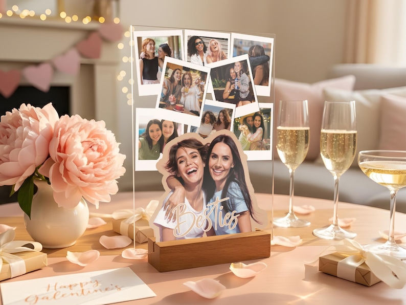 May include: A clear acrylic photo display stand with a wooden base featuring a collage of various candid photographs and a larger cutout image of two smiling individuals with the word Besties written in white script across the front surface.