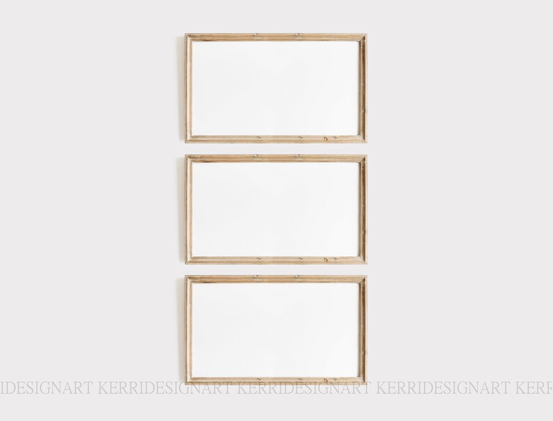 Op de afbeelding: Drie rechthoekige houten fotolijsten met een lichtbruine afwerking zijn verticaal tegen een witte muur geplaatst. Elke lijst heeft een wit interieur, klaar voor kunstwerken of foto's. De lijsten zijn leeg.